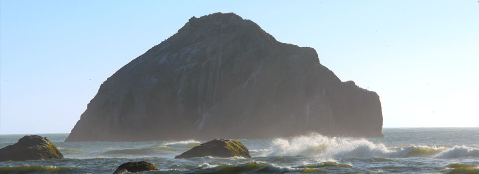 Face Rock rising from the surf, backlit by the afternoon sun